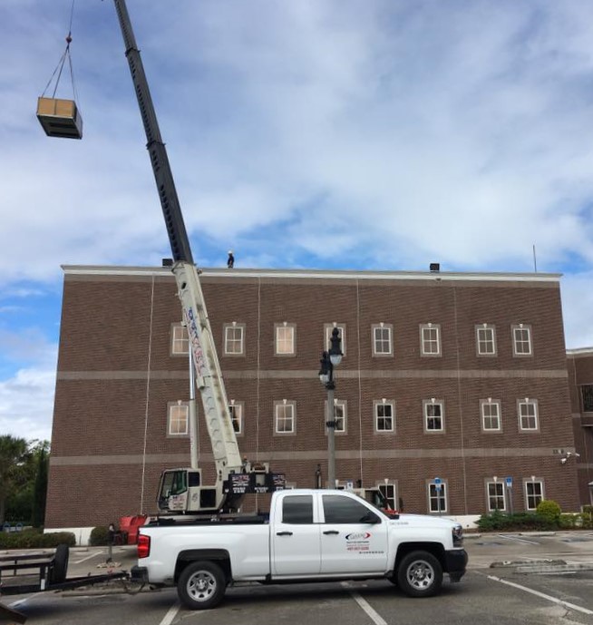 Huff's Quality Air Conditioning Inc truck lifting big box with a crane.